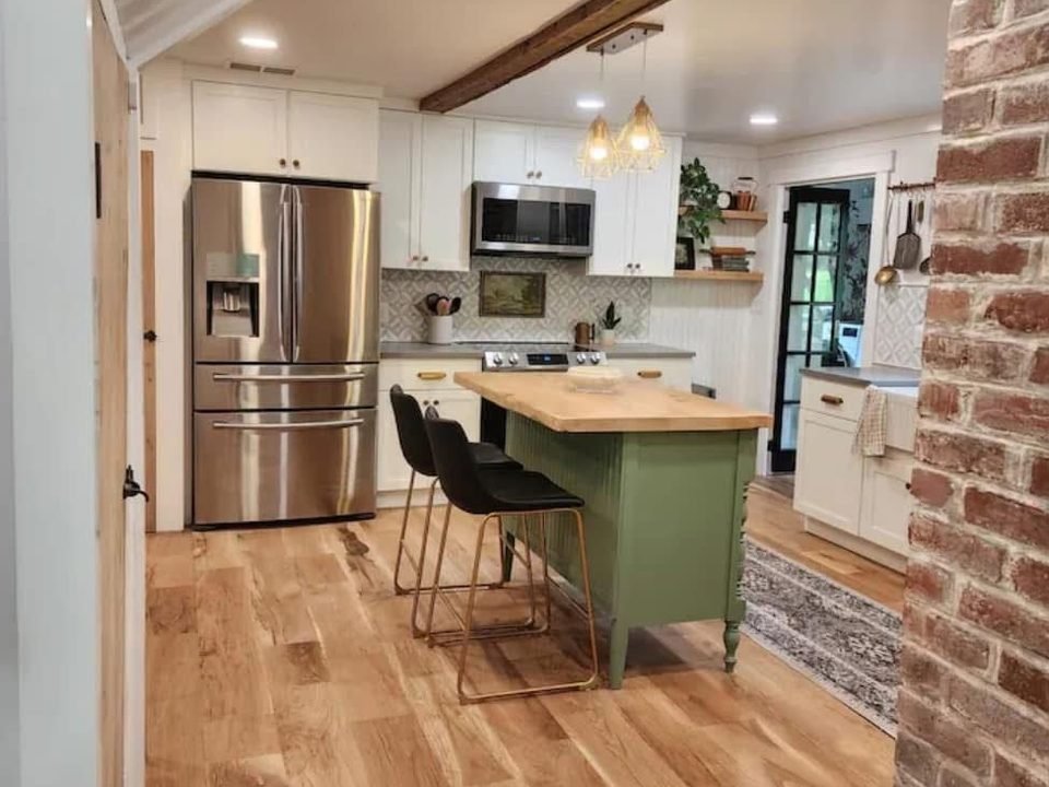 Kitchen with a green island, white cabinets and wood floors